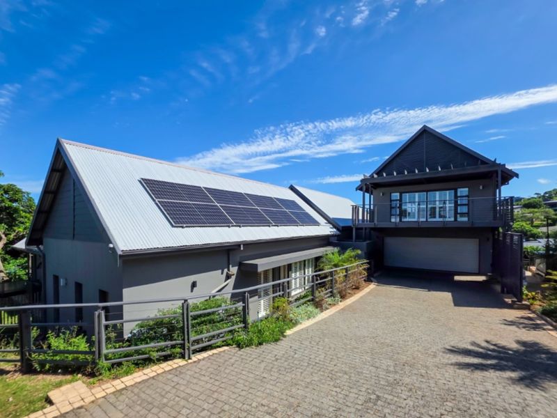 Modern multi-level home featuring a metal roof with integrated solar panels, a paved driveway, and an attached garage with an upper-level balcony.