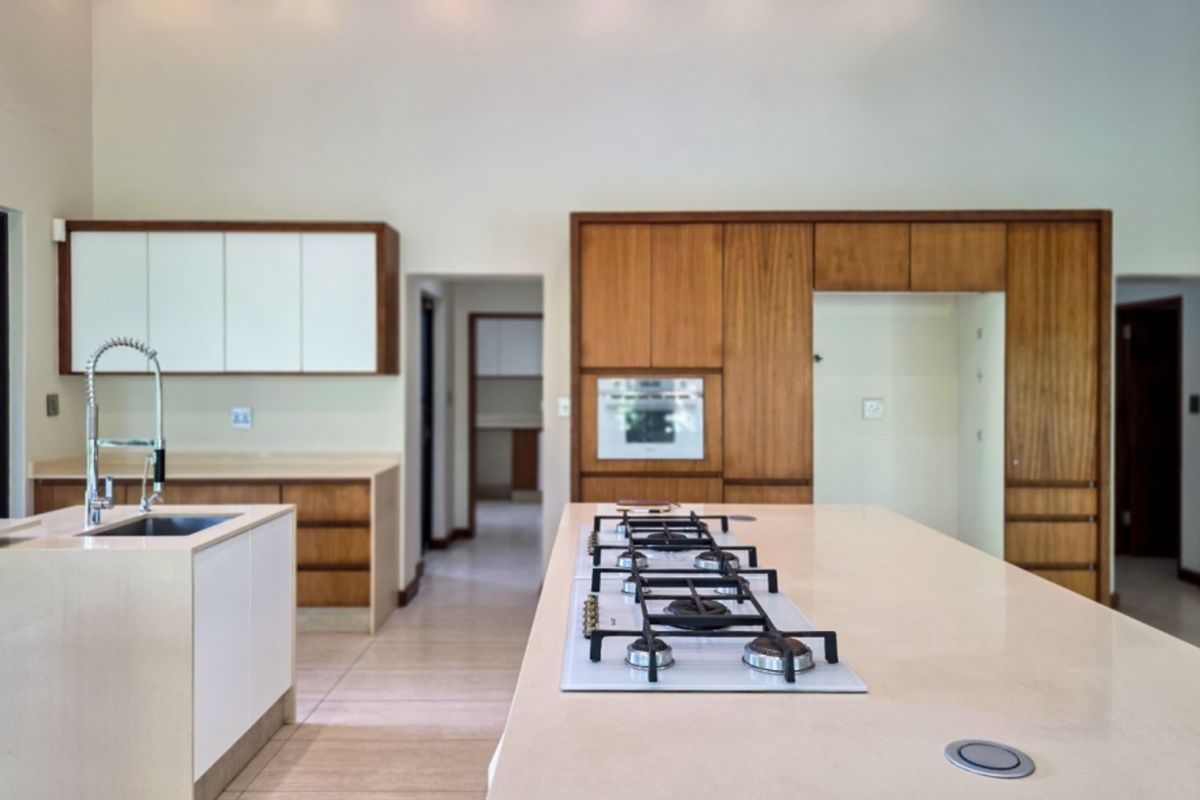 Modern kitchen featuring a large island with a gas cooktop, stone countertops, integrated cabinetry, and a secondary prep area visible in the background.