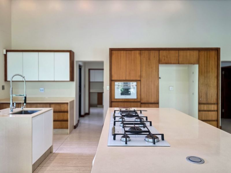 Modern kitchen featuring a large island with a gas cooktop, stone countertops, integrated cabinetry, and a secondary prep area visible in the background.