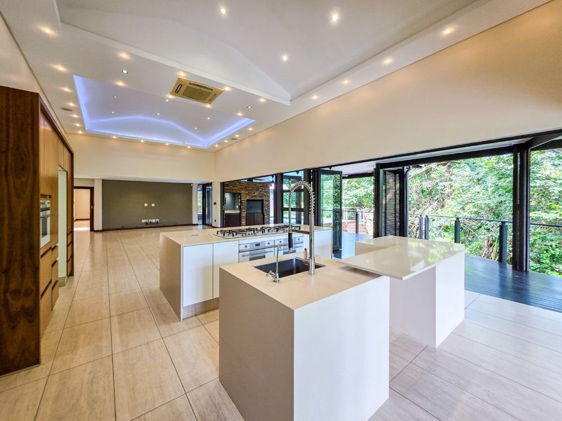 Spacious open-plan kitchen and living area featuring a modern island, high-end built-in appliances, recessed lighting, and seamless access to an outdoor deck.