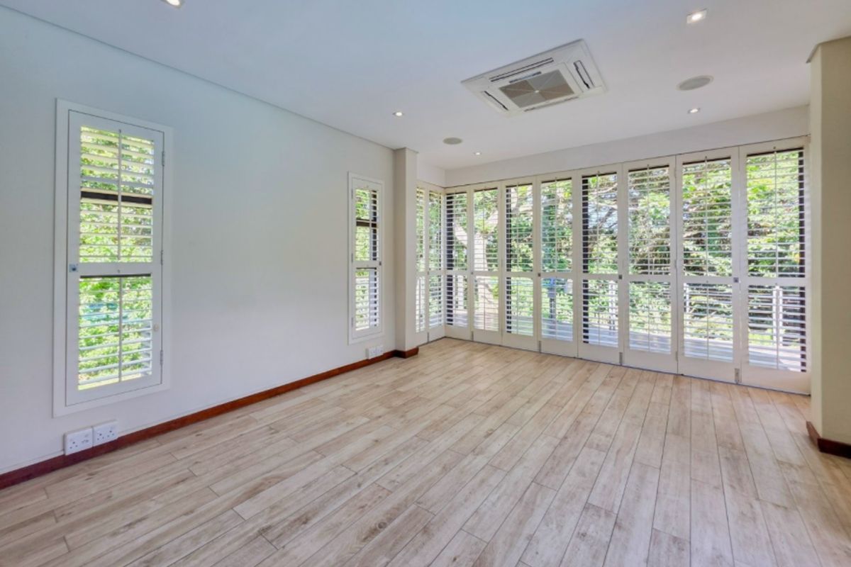 Bright and spacious living area featuring timber-look tile flooring, recessed lighting, ceiling-mounted air conditioning, and extensive plantation shutters with access to the outdoors.