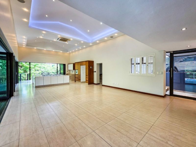 Spacious open-plan living and kitchen area featuring a modern tray ceiling with ambient lighting, tiled floors, and large sliding doors opening to the outdoors.