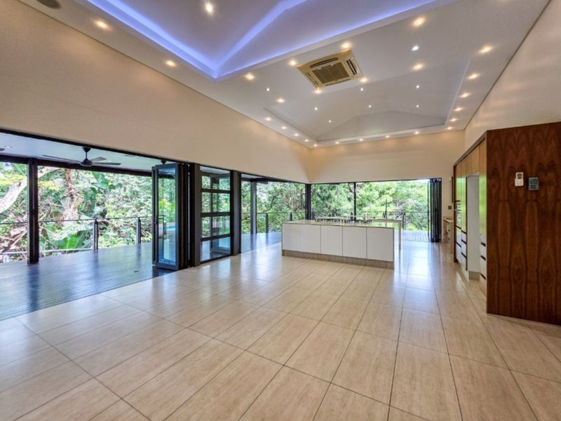 Spacious open-plan living and kitchen area featuring modern cabinetry, tiled floors, and expansive bi-fold doors opening onto a private deck with lush views.