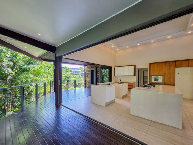 Spacious open-plan kitchen flowing onto a large timber deck with elevated views, featuring modern cabinetry, stone islands, and seamless indoor-outdoor integration.