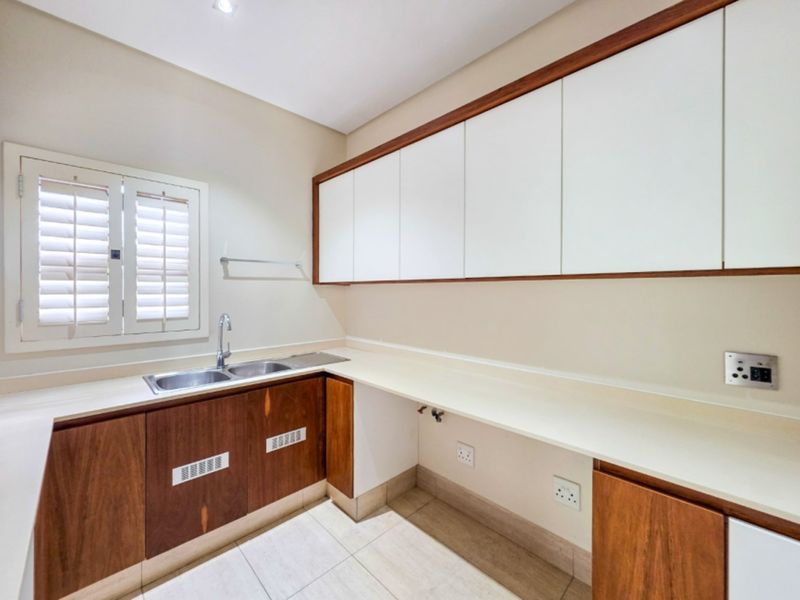 A clean and functional laundry room featuring built-in wooden cabinetry, a double stainless steel sink, and ample countertop space with tiled flooring.