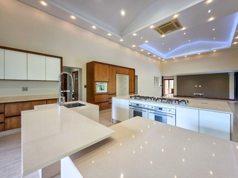 Spacious open-plan kitchen featuring a large island with stone countertops, integrated gas hob, built-in ovens, and modern recessed ceiling lighting.