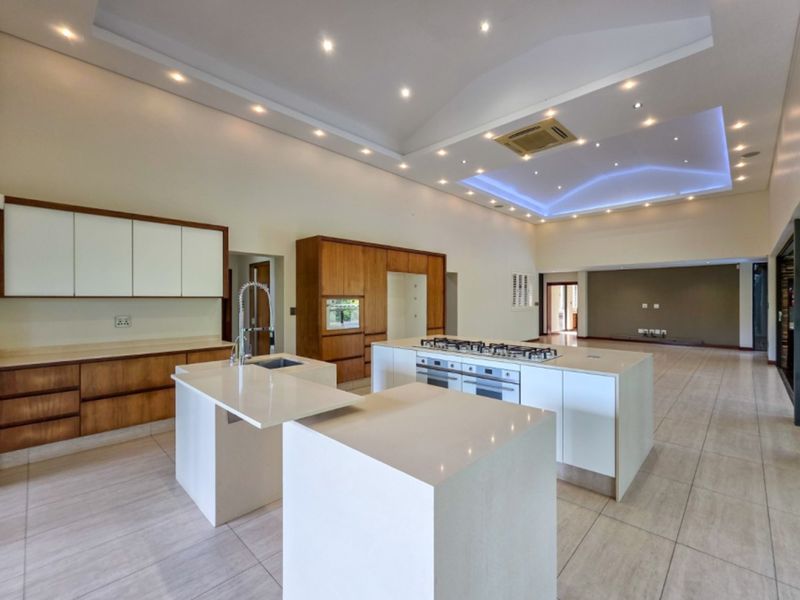 Spacious open-plan kitchen featuring modern cabinetry, stone countertops, dual islands, and integrated appliances under a high vaulted ceiling with ambient lighting.