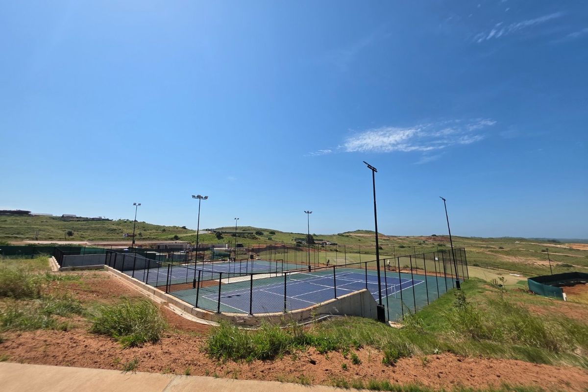 A well-maintained outdoor tennis court facility featuring dual courts, perimeter chain-link fencing, and integrated floodlighting, set within a landscaped residential estate.