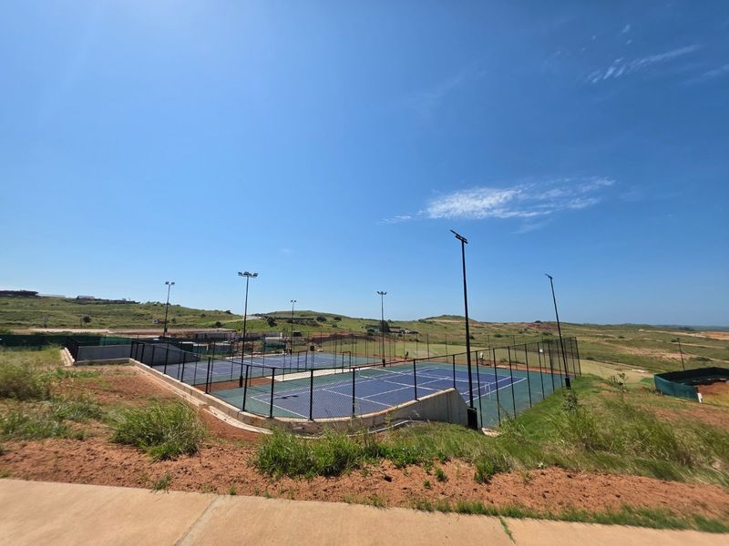A well-maintained outdoor tennis court facility featuring dual courts, perimeter chain-link fencing, and integrated floodlighting, set within a landscaped residential estate.