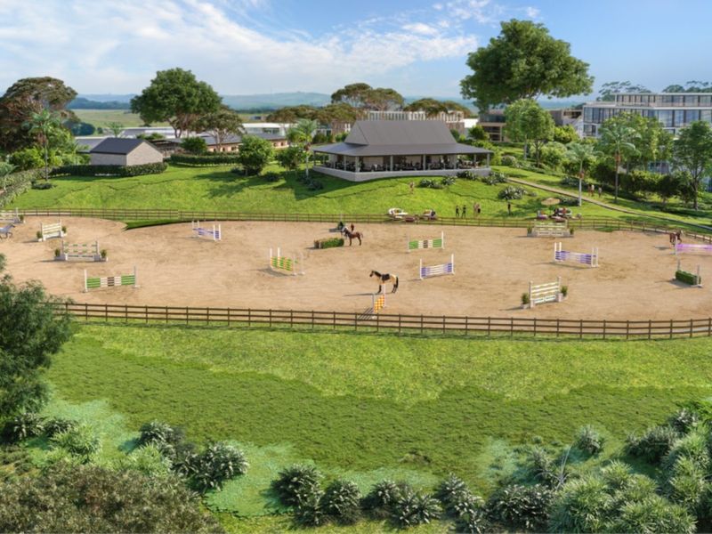 An aerial view of a professional equestrian arena featuring show jumping obstacles, post and rail fencing, and an adjacent clubhouse facility.