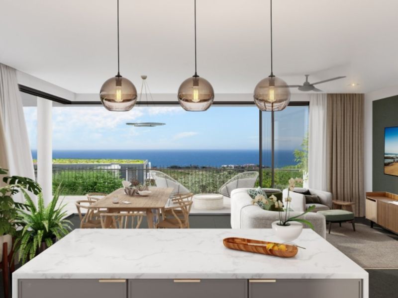 Modern open-plan living area featuring a sleek kitchen island, pendant lighting, and expansive sliding doors opening to a scenic ocean view balcony.