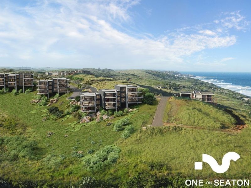 An aerial perspective of a modern coastal apartment development set within a natural landscape, showcasing the architectural layout and proximity to the ocean.