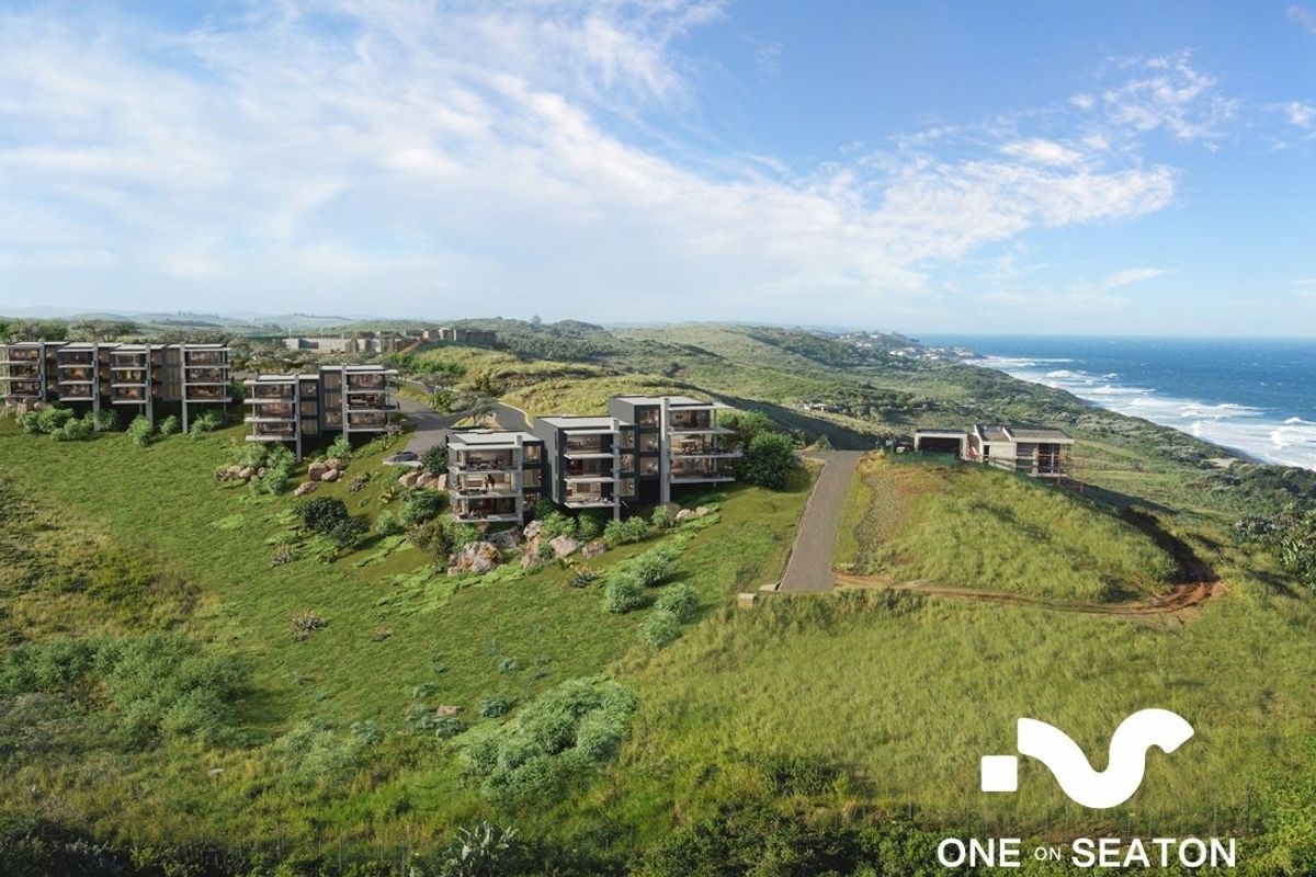 An aerial perspective of a modern coastal apartment development set within a natural landscape, showcasing the architectural layout and proximity to the ocean.