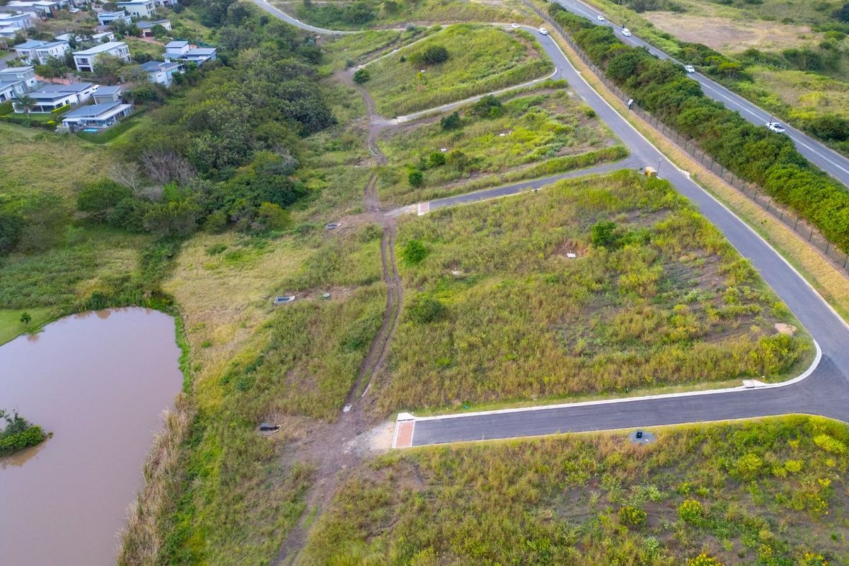 Aerial view of a vacant residential land parcel featuring established road access, drainage infrastructure, and proximity to a natural pond and surrounding residential development.