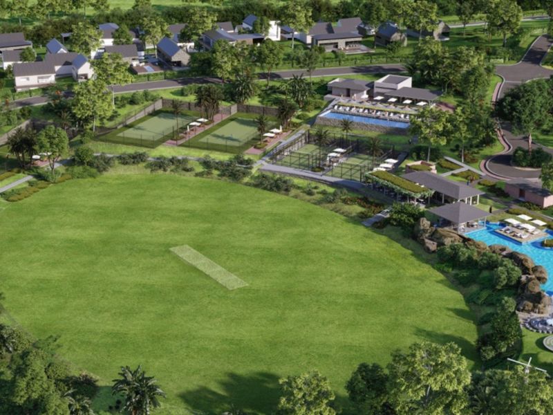 Aerial view of a residential estate featuring a cricket pitch, tennis courts, swimming pool, clubhouse, and landscaped communal areas.