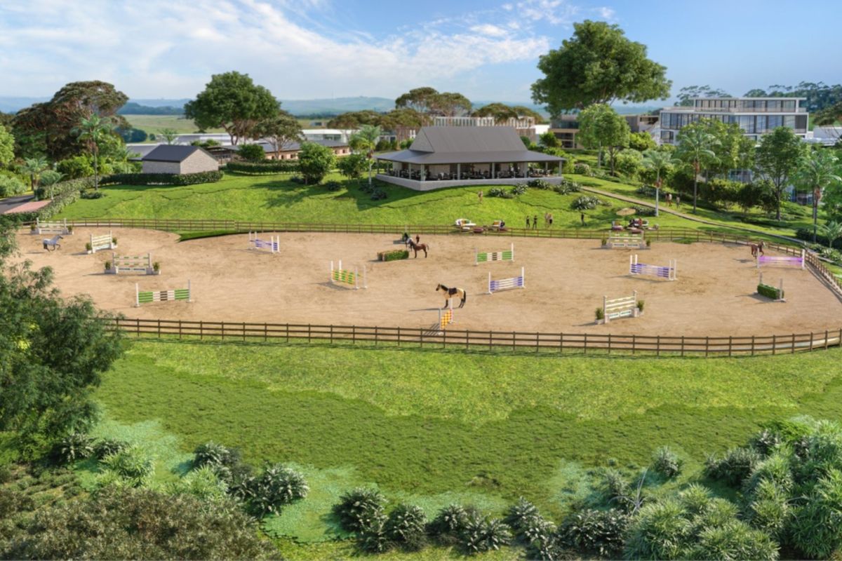 An aerial view of a professional equestrian arena featuring show jumping obstacles, post and rail fencing, and an adjacent clubhouse facility.
