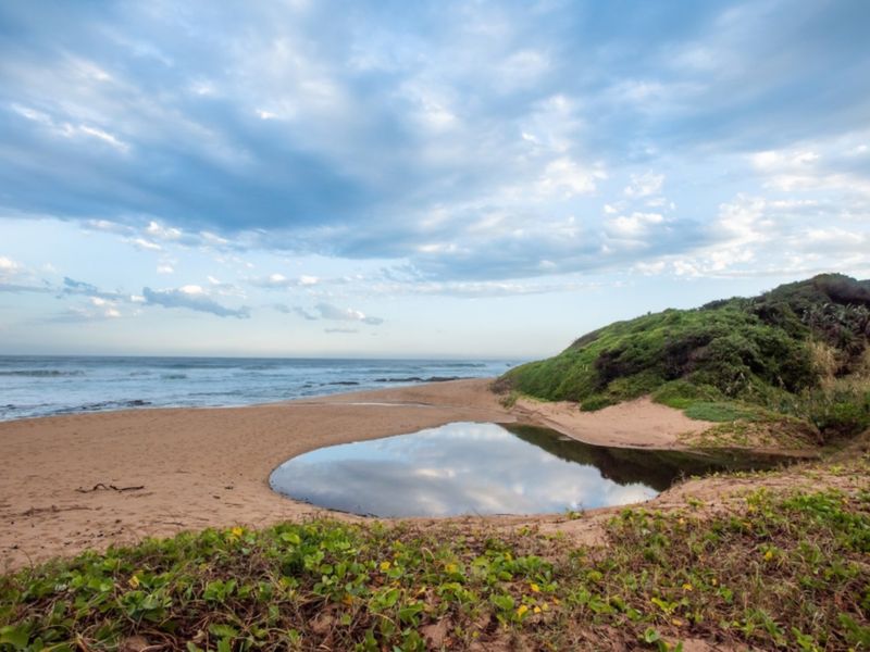 A scenic view of the coastal landscape featuring a sandy beach, natural tidal pool, and ocean horizon.