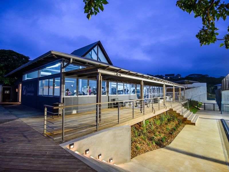 Modern clubhouse facility featuring extensive timber decking, covered veranda, and architectural lighting, set within a well-maintained estate environment.