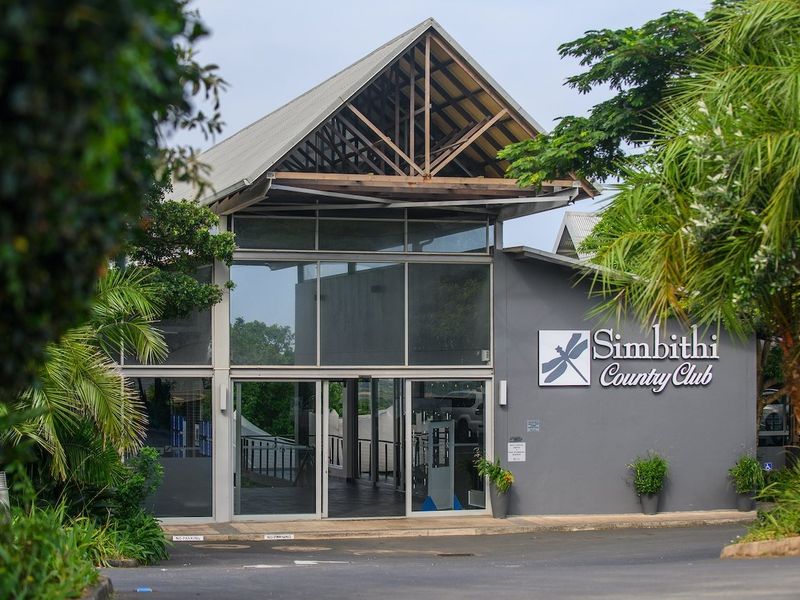 The front entrance of the Simbithi Country Club featuring a modern architectural design with large glass panels and an exposed timber roof structure.
