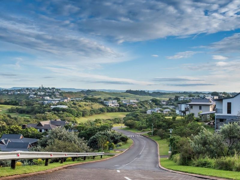 A scenic view of a paved residential street winding through a well-maintained estate with surrounding greenery and hillside homes.