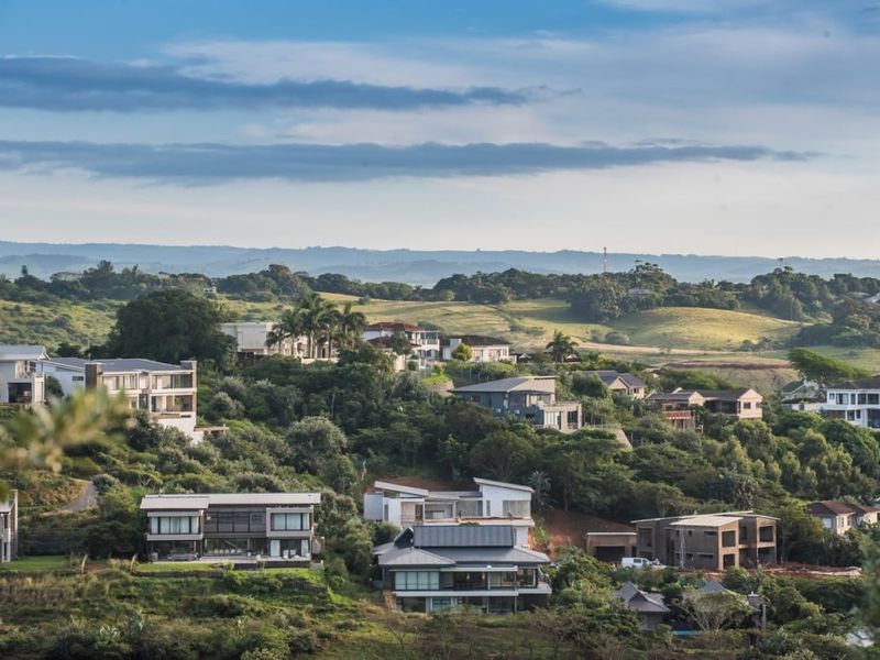 A scenic elevated view overlooking a residential estate with modern homes nestled within a lush, hilly landscape.