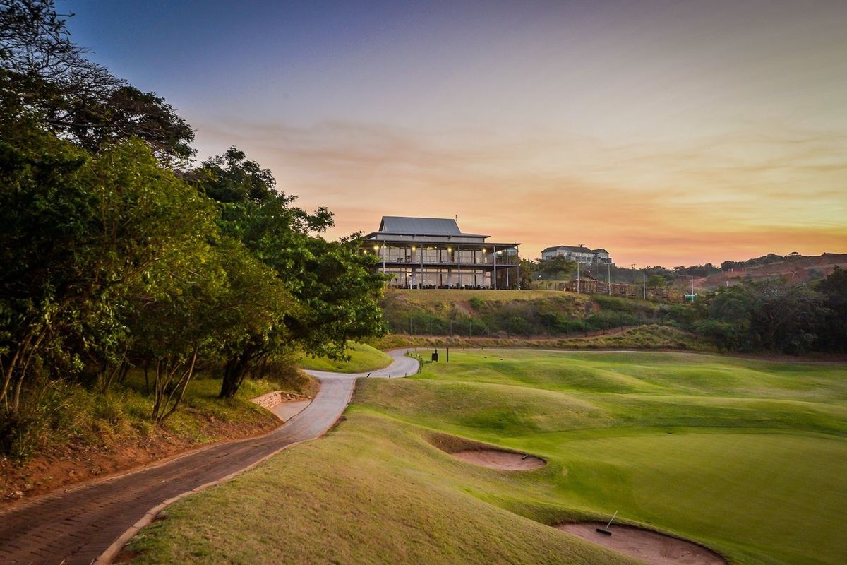 A scenic view of a well-maintained golf course with a paved cart path leading toward a clubhouse at sunset.