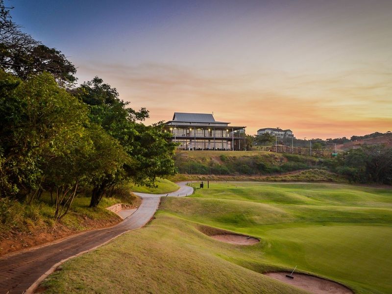 A scenic view of a well-maintained golf course with a paved cart path leading toward a clubhouse at sunset.