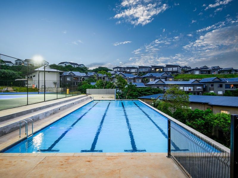 A well-maintained communal swimming pool and adjacent tennis court facility within a residential estate setting.