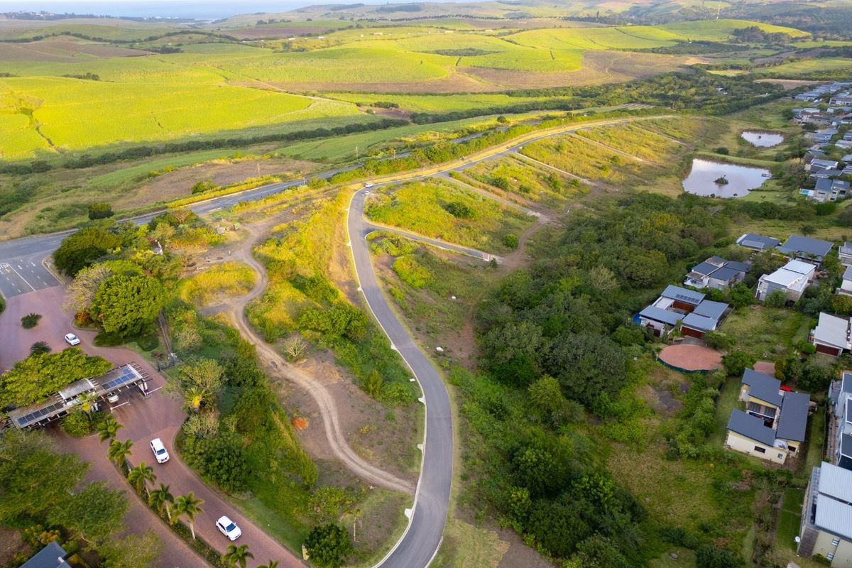 Aerial view of a residential development site featuring paved access roads, established greenery, and surrounding agricultural landscape.