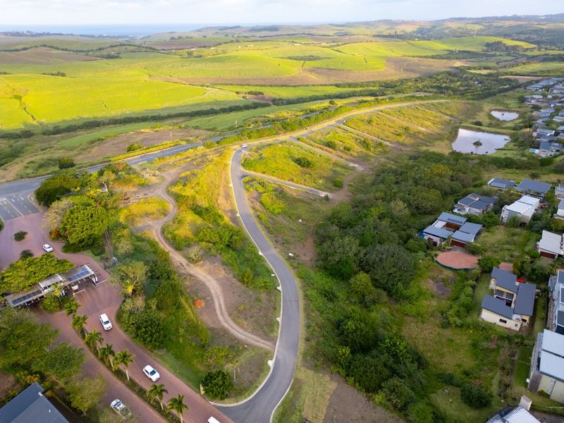 Aerial view of a residential development site featuring paved access roads, established greenery, and surrounding agricultural landscape.