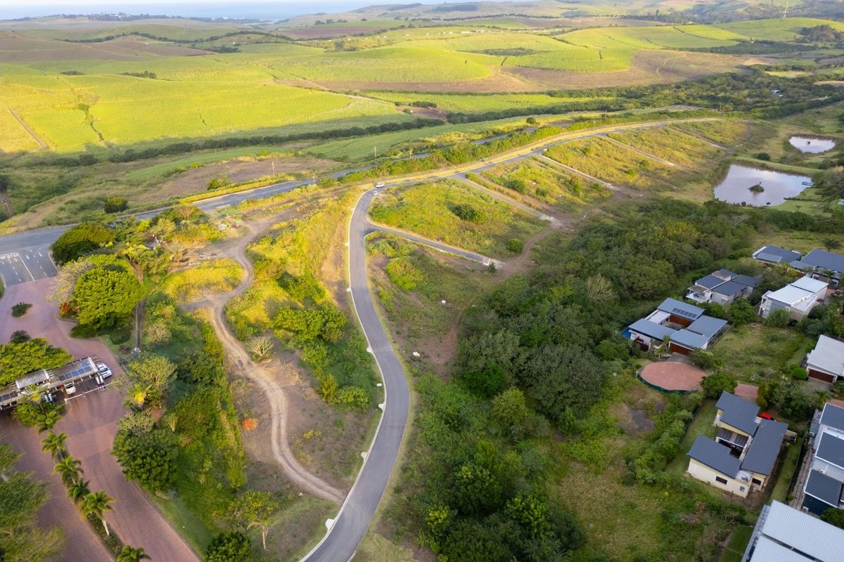 Aerial view of a vacant residential land parcel featuring established road access and surrounding natural landscape in a developing estate.