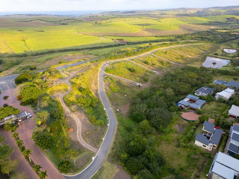 Aerial view of a vacant residential land parcel featuring established road access and surrounding natural landscape in a developing estate.