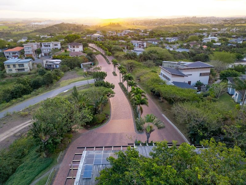 Aerial view of a well-maintained residential estate featuring paved roads, lush landscaping, and surrounding homes at sunset.