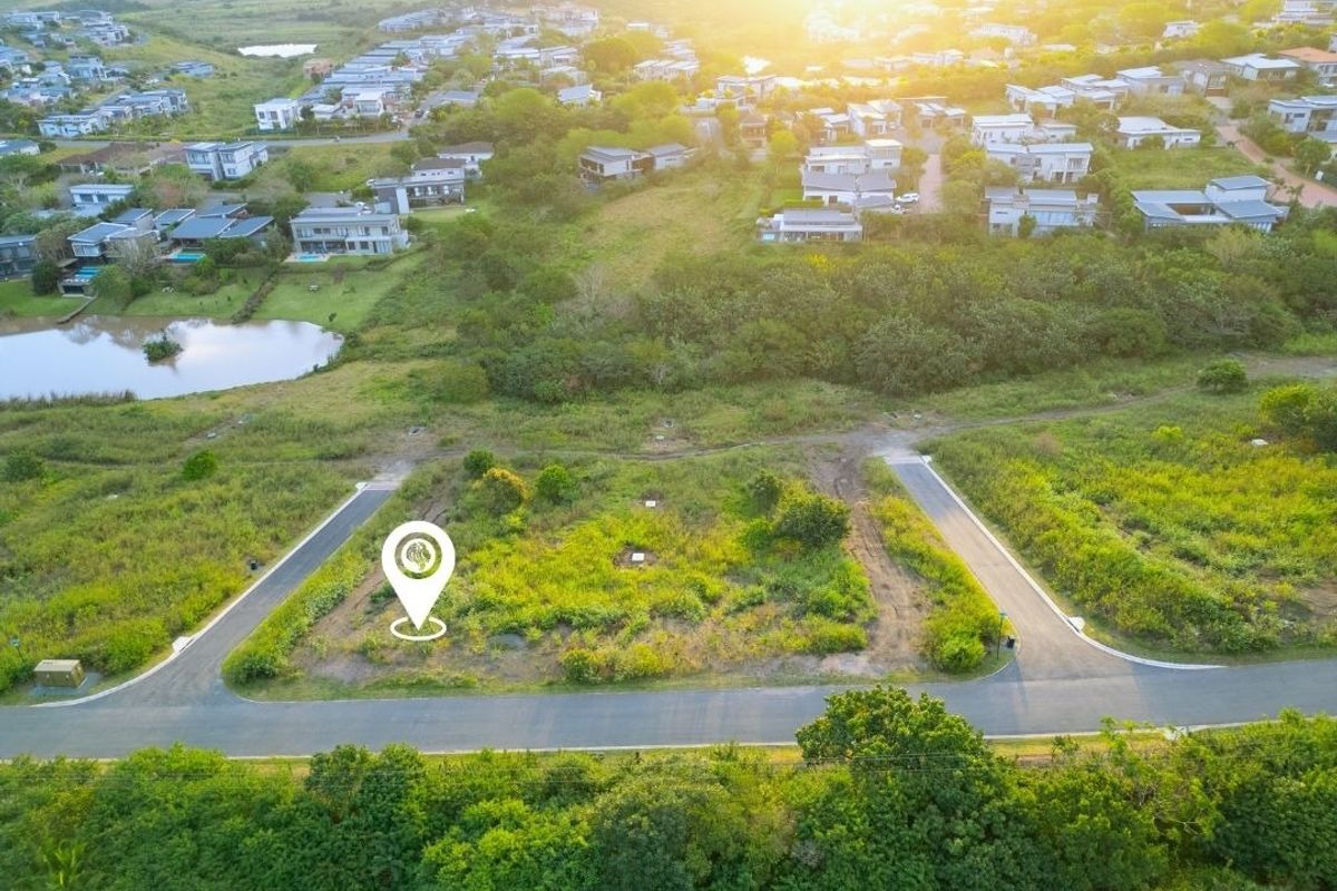 An aerial view of a vacant residential plot situated within a developed estate, featuring road access and surrounding greenery.