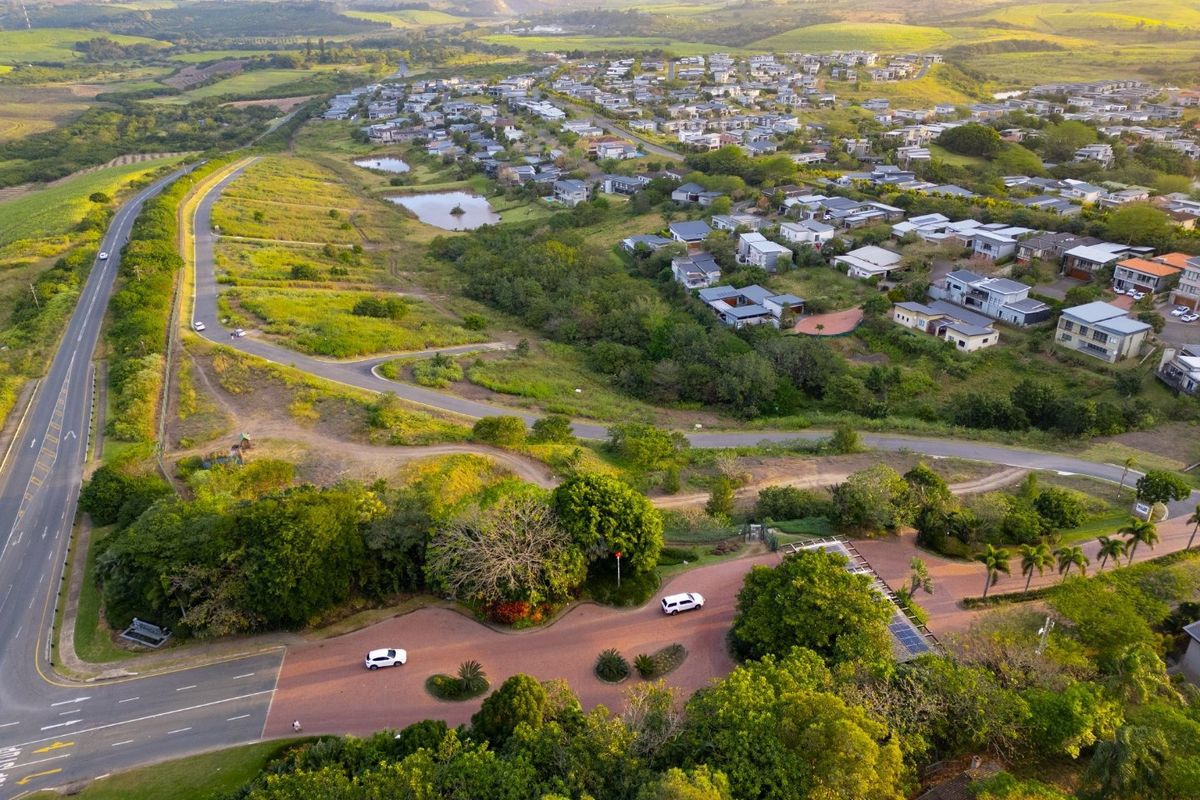 Aerial view of a residential estate entrance and surrounding landscape, showcasing the development layout and access roads.