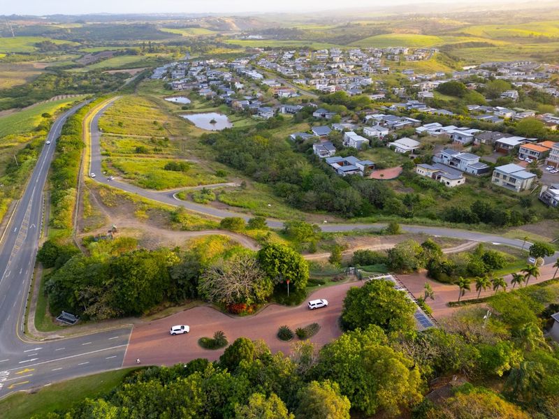 Aerial view of a residential estate entrance and surrounding landscape, showcasing the development layout and access roads.