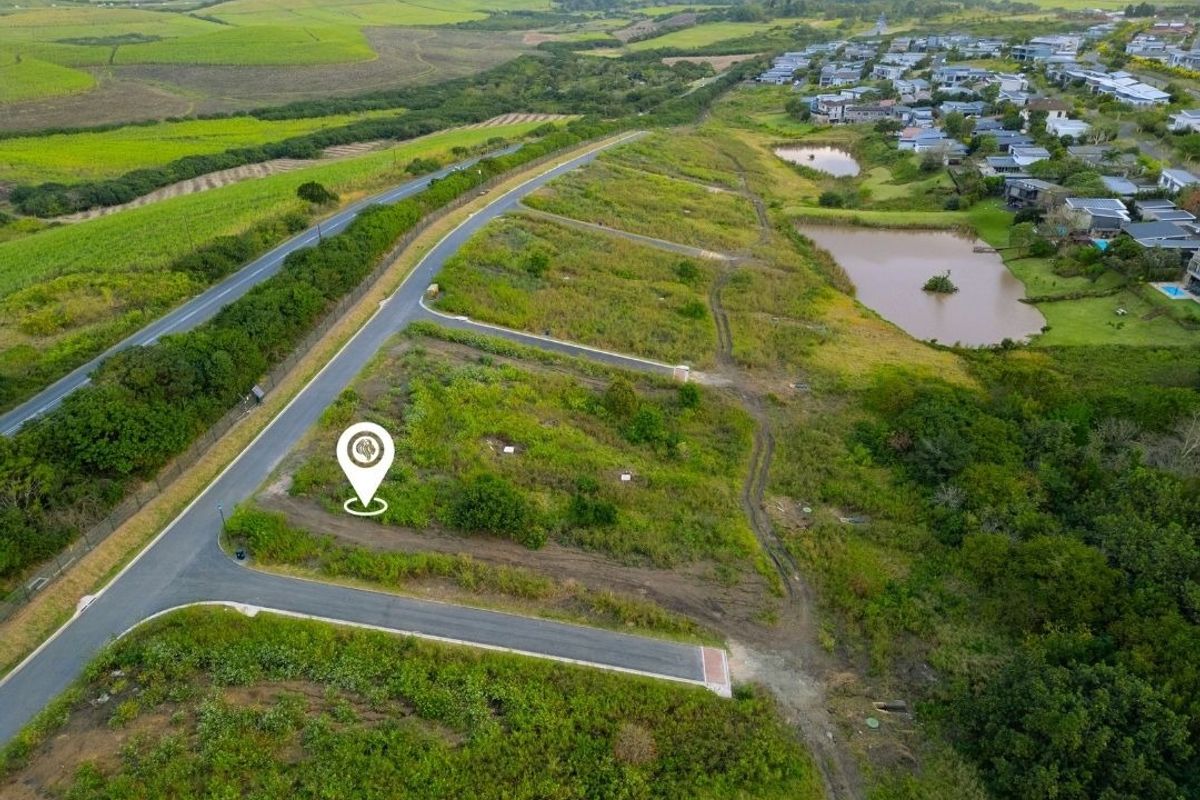 Aerial view of a vacant residential plot in a developed estate, featuring established road infrastructure and surrounding green landscape.
