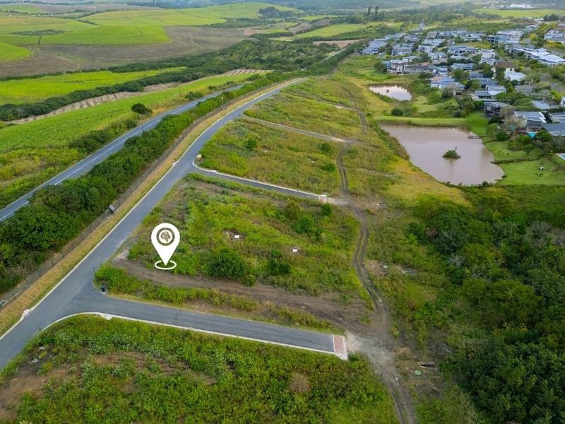 Aerial view of a vacant residential plot in a developed estate, featuring established road infrastructure and surrounding green landscape.