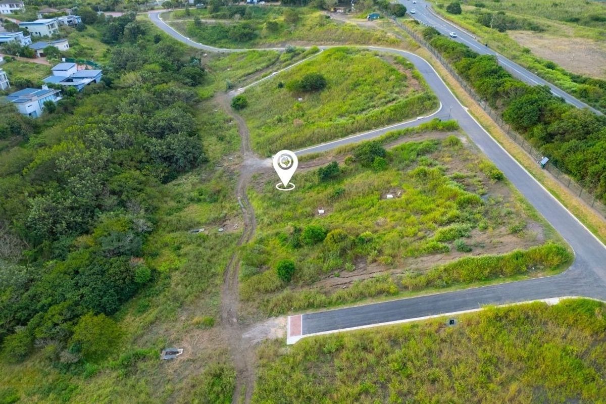 An aerial view of a vacant residential plot featuring established road access and surrounding natural landscape in a developing estate.