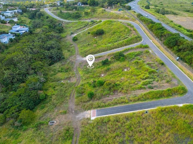 An aerial view of a vacant residential plot featuring established road access and surrounding natural landscape in a developing estate.
