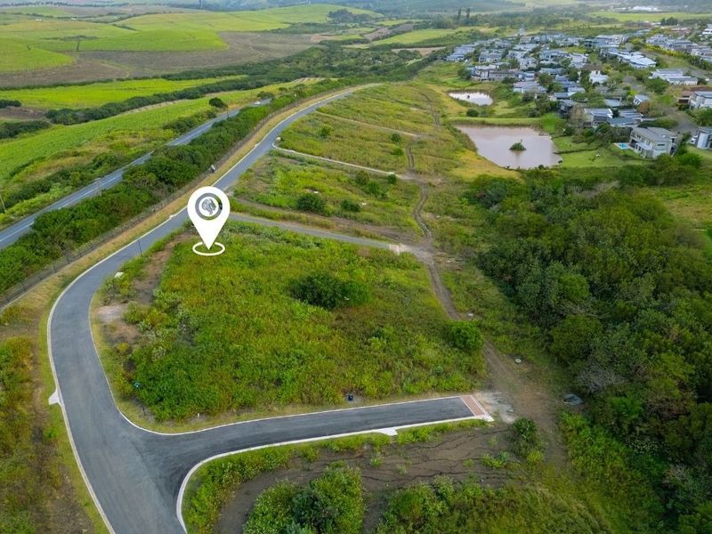 Aerial view of a vacant residential plot situated in a developed estate with paved road access and surrounding green space.
