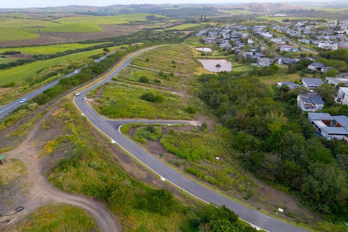 Aerial view of a vacant residential plot featuring paved road access and surrounding natural landscape within a developed estate.