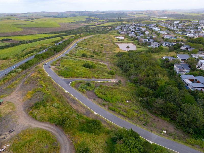 Aerial view of a vacant residential plot featuring paved road access and surrounding natural landscape within a developed estate.