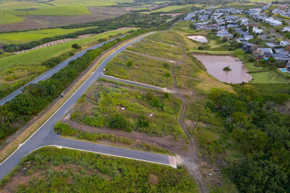 Aerial view of a residential vacant land development featuring paved access roads, utility connections, and proximity to established residential areas and natural landscape.