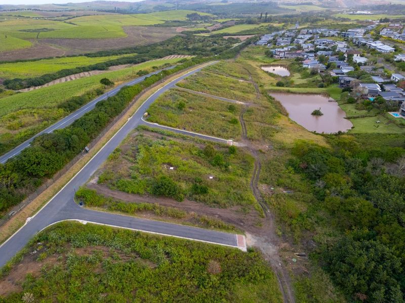 Aerial view of a residential vacant land development featuring paved access roads, utility connections, and proximity to established residential areas and natural landscape.