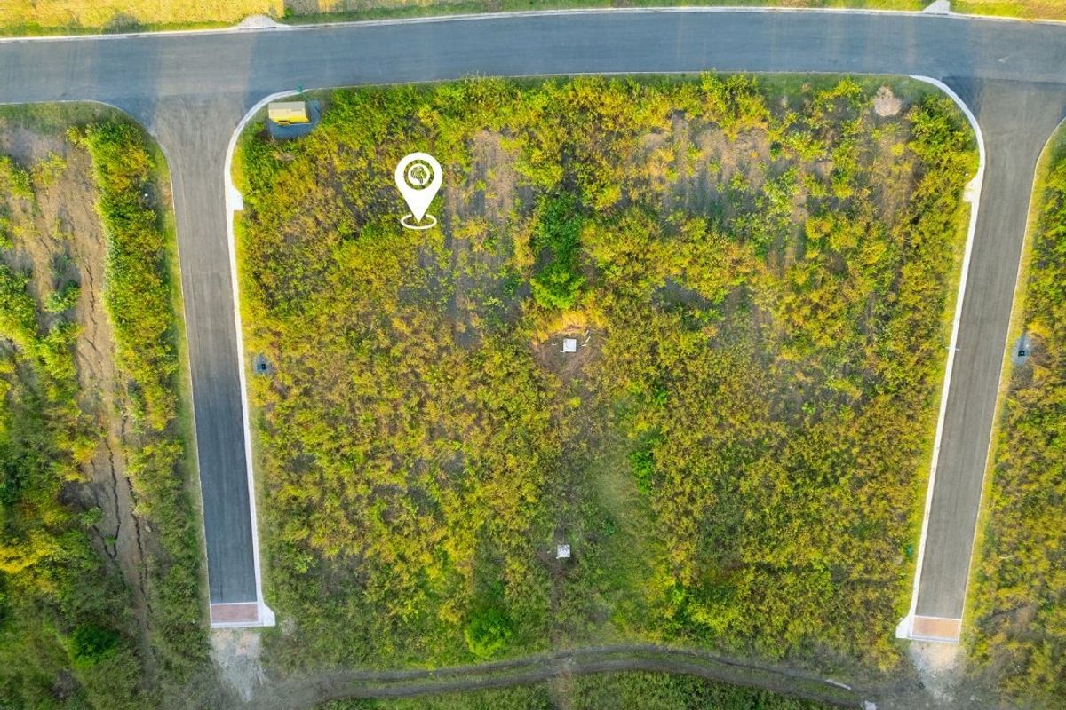 Aerial view of a vacant residential plot featuring road access and established utility connection points, ready for development.
