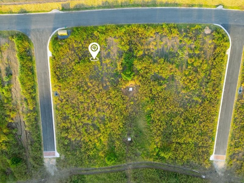 Aerial view of a vacant residential plot featuring road access and established utility connection points, ready for development.