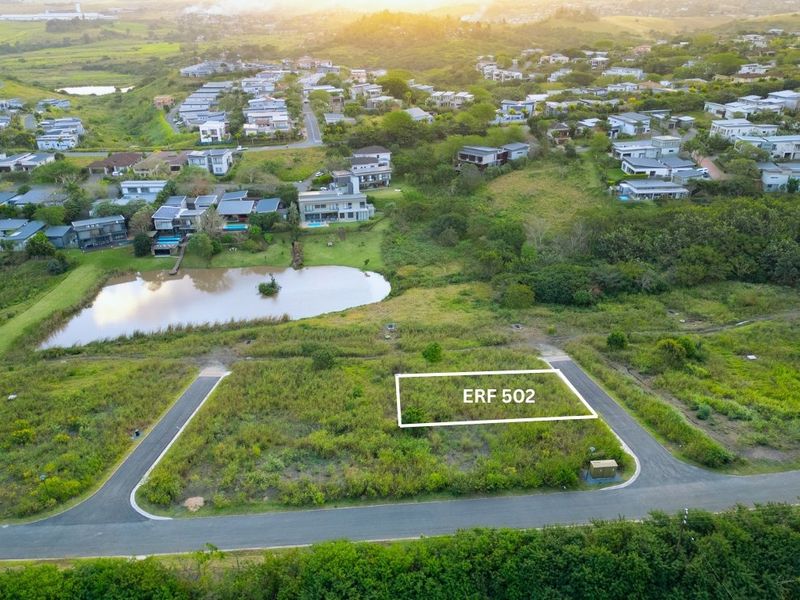 Aerial view of a vacant residential plot, ERF 502, situated in a developed estate with road access and nearby pond.