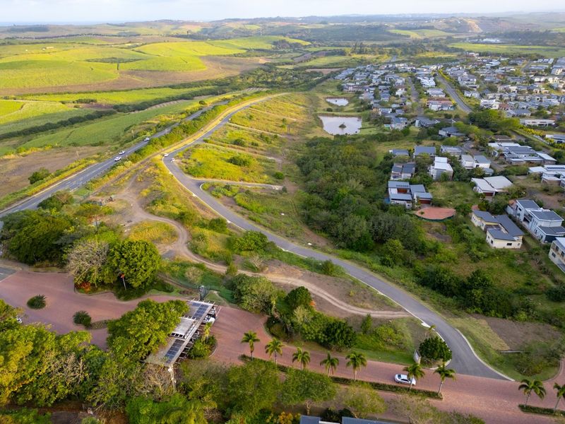 Aerial view of a residential estate featuring paved roads, landscaped surroundings, and proximity to surrounding greenbelt areas and existing housing developments.