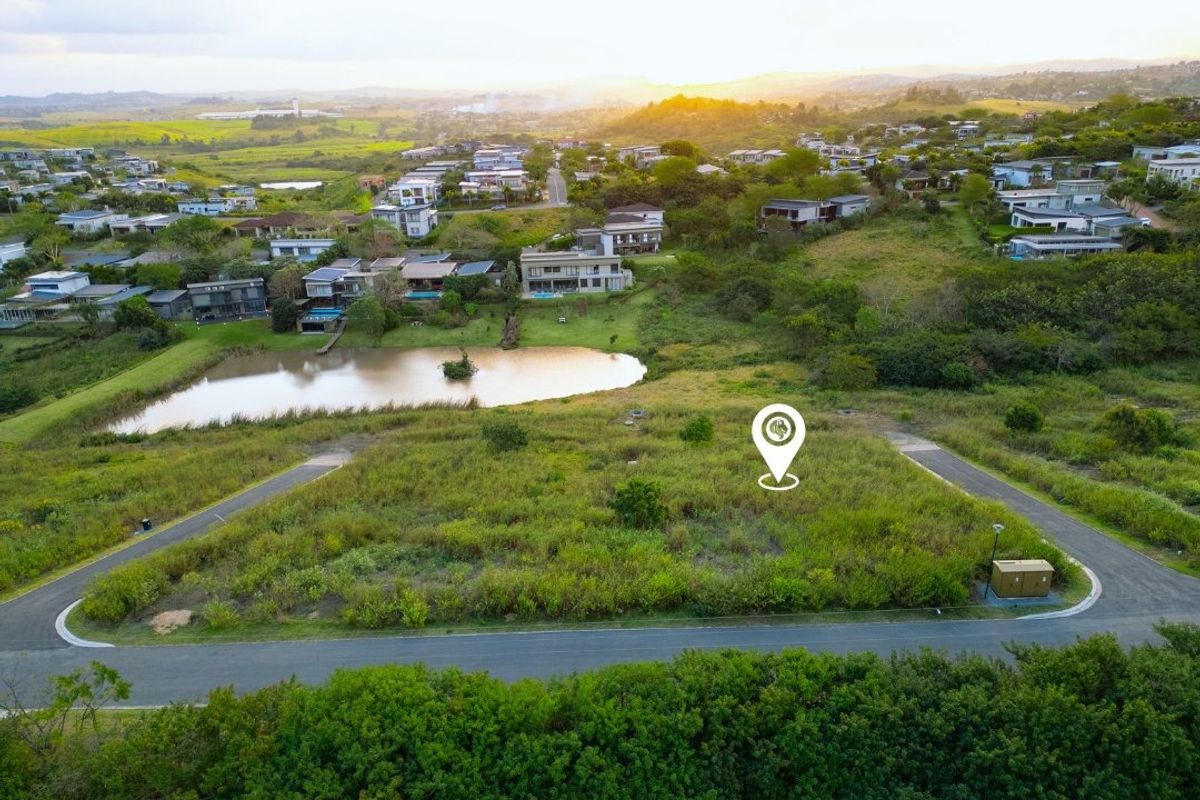 Aerial view of a vacant residential plot featuring road access and proximity to a scenic pond within a developed estate.
